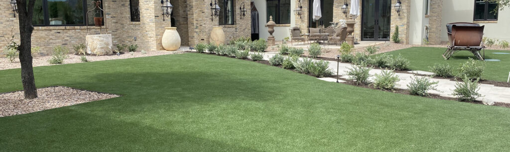 Spacious backyard with a manicured lawn, trimmed hedges, and stone pathway. The brick building features large windows. Decorative pots and outdoor furniture enhance the cozy ambiance.
